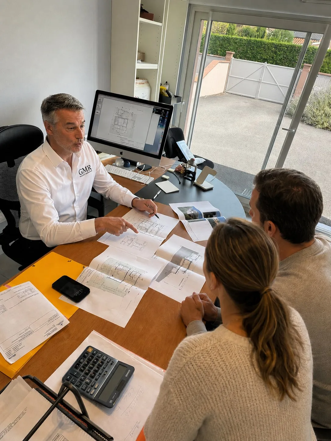 Richard Gamero présentant des plans à des clients dans les bureaux de GMR Projets Immobiliers.
